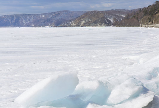 Transparent blue ice hummocks on lake Baikal shore. Siberia winter landscape view. Snow-covered ice of the lake. Big cracks in the ice floe.