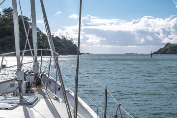 Obraz premium Sailboat yacht motoring out of Tutukaka Harbour between rocks and navigational channel marker in Northland, New Zealand, NZ