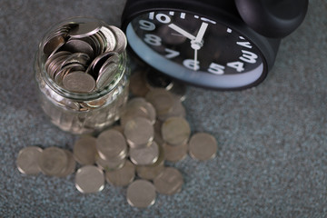 Alarm clock and step of coins stacks with coin in glass jar on working table, time for savings money concept.