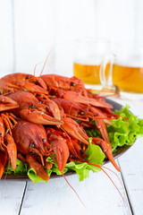 A large pile of boiled crawfish on a ceramic plate,  glasses of beer on a white wooden background.