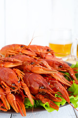 A large pile of boiled crawfish on a ceramic plate,  glasses of beer on a white wooden background.