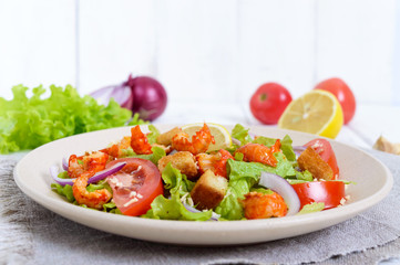 Light tasty salad with meat of a cancer, shrimps, lettuce, garlic croutons, tomatoes, red onions on a white background.
