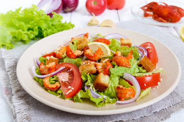 Light tasty salad with meat of a cancer, shrimps, lettuce, garlic croutons, tomatoes, red onions on a white background.