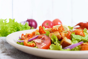 Light tasty salad with meat of a cancer, shrimps, lettuce, garlic croutons, tomatoes, red onions on a white background.