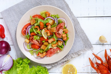 Light tasty salad with meat of a cancer, shrimps, lettuce, garlic croutons, tomatoes, red onions on a white background. The top view