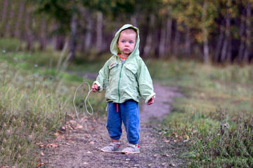 A one-and-a half year old girl on a path in a park with a rope in her hand. The girl looks aside....
