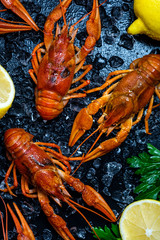 Fresh boiled crawfish with lemons and greens on a dark table with ice.