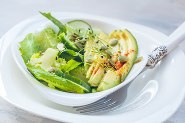 Green salad with broccoli, sprouts and avocado, light background