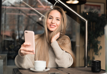 Beautiful woman is doing selfie using a smart phone and smiling while resting in cafe