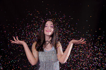 A young girl stands in front of a black background and is surrounded by confetti explosions. She laughs and smiles in her role as the party girl.