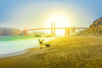 Papier Peint photo Plage de Baker, San Francisco Homme jouant avec son chien à Baker Beach au coucher du soleil avec Golden Gate Bridge. Touristes marchant sur le rivage. Vacances, voyages et loisirs à San Francisco, Californie, États-Unis.