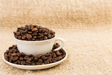 Coffee cup filled with roasted beans on jute text area