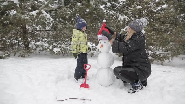 Mom and son make a snowman 7 Happy mother and son make a snowman falling fluffy snow