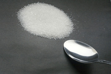 Sugar drug of our time. The spoon next to the hill of the white beet sugar