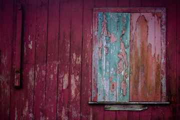 Old grunge and weathered home facade with green window and red wall planks texture background marked by long exposure to the elements outdoors.