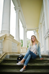 Fototapeta premium Blonde girl wear on jeans with backpack posed against vintage house.