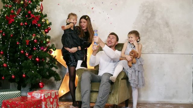 Happy father, mother and two daughters celebrating Christmas together. Cute family of four having fun with petards sitting by the decorated Christmas tree