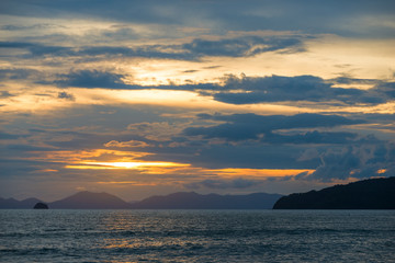 Fototapeta premium beautiful clouds and orange sunset over the sea, mountains on the horizon