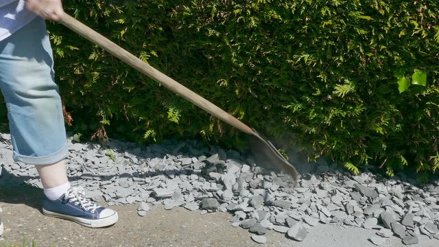 Dolly shot of a woman raking decorative stone chippings in her garden, in order to level them out.
