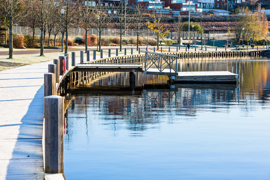Wooden combo pier with three sections. A normal pier with a bridge and railings and the last part is a floating pier. Water is calm and the boardwalk frosty. Location Vaxjo, Sweden.