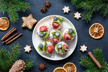 Christmas sweets, canape tartlets or cupcakes with cream and berries on white plate. Gingerbread cookies and festive decorations frame. Winter holidays food. New Year sweet food. Top view