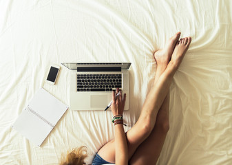 View from above of a woman using her laptop and smartphone on the bed. 