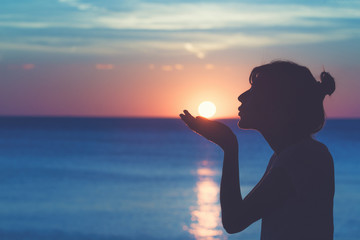 Silhouette of a girl kissing the sun with ocean / sea sunny background.