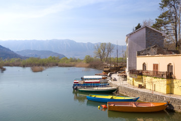 Fototapeta na wymiar bright boats on lake near house on background of mountain