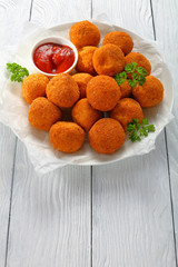 tasty potato croquettes - mashed potatoes balls breaded and deep fried, served with ketchup on white plate, vertical view from above