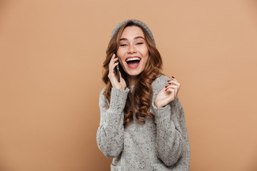 Fototapeta premium Portrait of beautiful laughing brunette woman in warm clothes talking on mobile phone, looking at camera