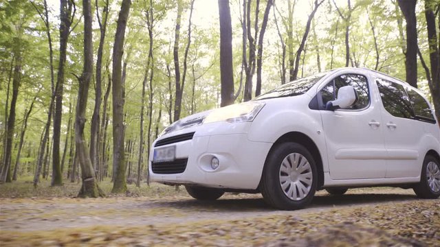 Front side of white minivan vehicle while driving in forest 4K