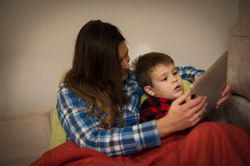 Mother and son sitting on sofa using digital tablet.