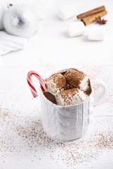 Cup of traditional hot chocolate with marshmallows and candy cane on white table.