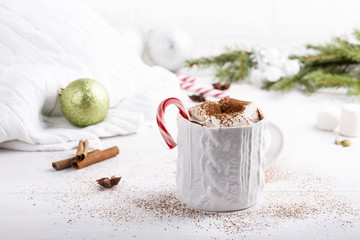 Cup of traditional hot chocolate with marshmallows and candy cane on white table.