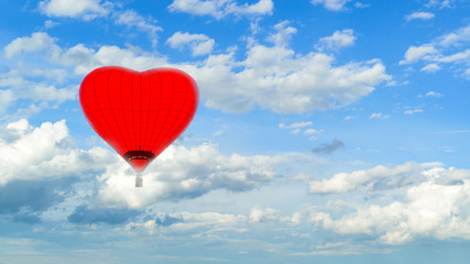 Obraz premium Hot air red ballon in the shape of heart against blue sky with white fluffy clouds and copyspace for text