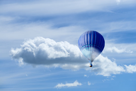Hot air blue ballon against blue sky with white fluffy clouds and copyspace for text