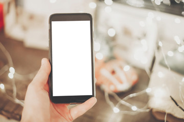 hand holding smart phone with empty screen on background of christmas lights in evening. space for text. happy holidays. black friday sale. vintage tone. merry christmas greetings
