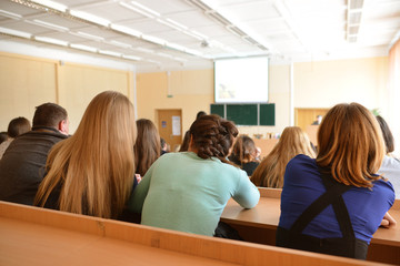 Rear view of students sitting and listening in lecture hall, selective focus