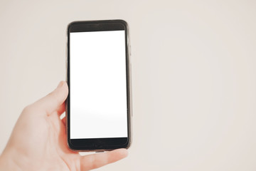 hand holding smart phone with empty screen on background of white wall. space for text.