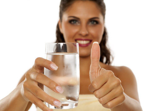 young woman holding a glass of cold mineral water and showing thumbs up