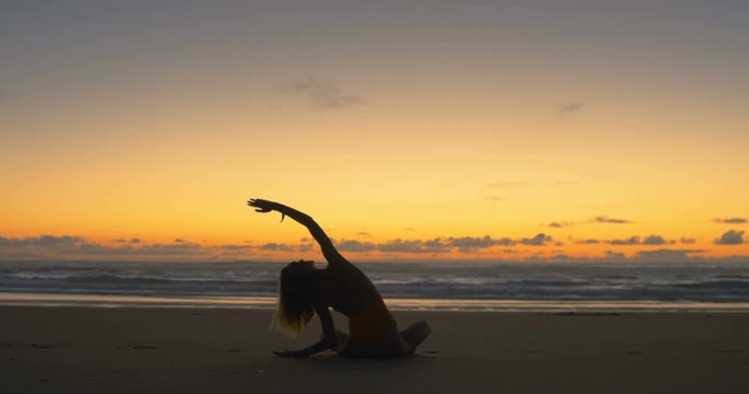 Silhouette of Beautiful Young Woman in the Swimsuit Doing Sitting Yoga on the Beach while Watching the Sunset. Girl Has Blond Hair, is Very Slim and Attractive. She Meditates and Looks at the Ocean.