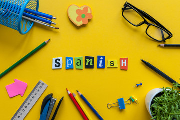 SPANISH made with carved letters on yellow desk with office or school supplies, stationery. Concept of Spanish language courses