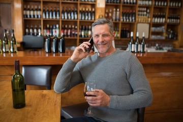 Smiling senior man talking on mobile phone while having red wine