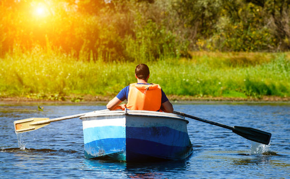 Man in life jacket rowing a boat over clear water on the river in rays of the sun