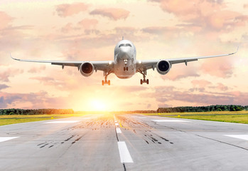 Passenger airplane landing at sunset on a runway.