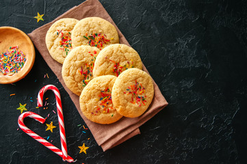 American style round cookies with confetti (shortbread) on a napkin and heart shaped candy cane on a black stone backdrop.