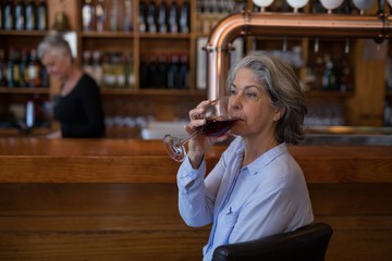 Senior woman having glass of red wine at counter