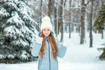 Fototapeta na wymiar A girl dressed in warm winter clothes and a hat posing in a winter forest. Model with a beautiful smile near the Christmas tree.