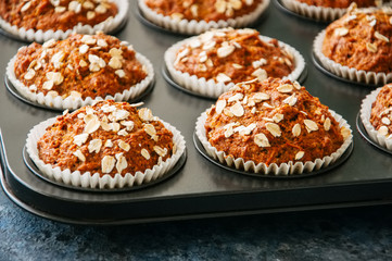 Carrot cake muffins with nuts, raisins and oats on a blue stone background.