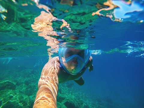 Underwater photo of a young handsome man swimming in the turquoise exotic sea near the surface with snorkelling mask and looking at the camera for summer vacation.